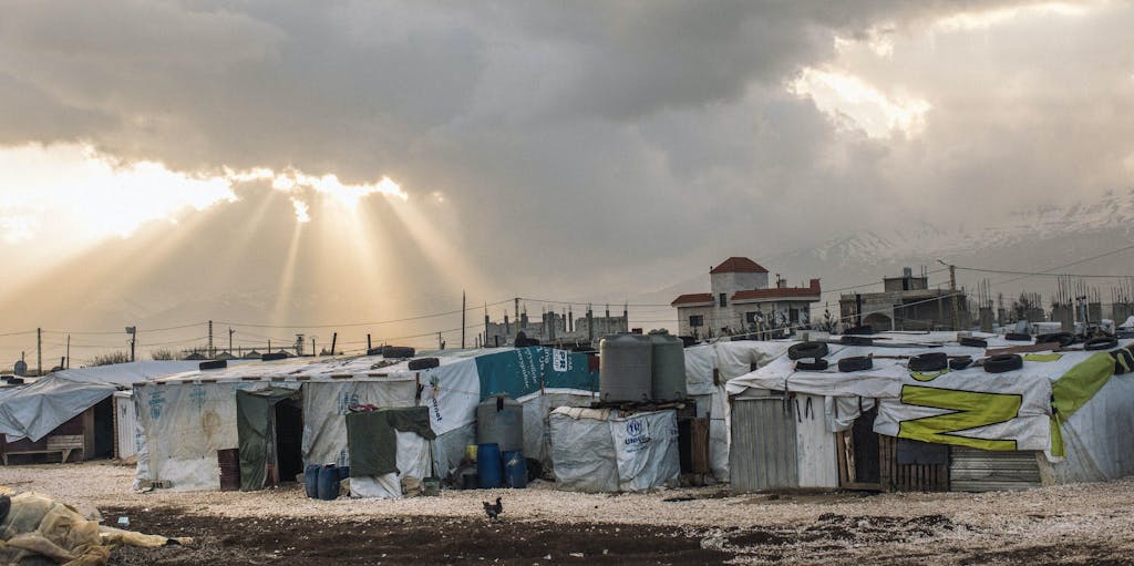 Landscape photo of gray rain clouds and light peaking through over a gray Syrian refugee camp in Lebanon, where FH is responding.