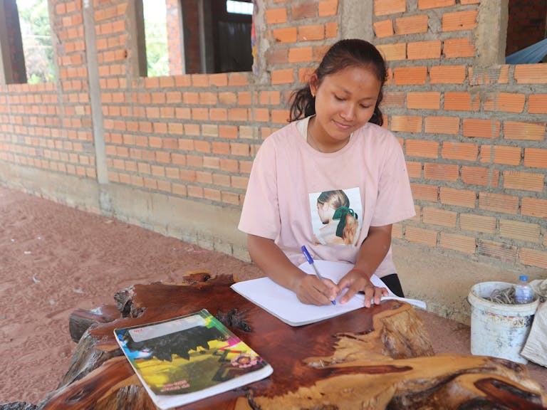 SreyMe writing in her school notebook as she works to further her education.
